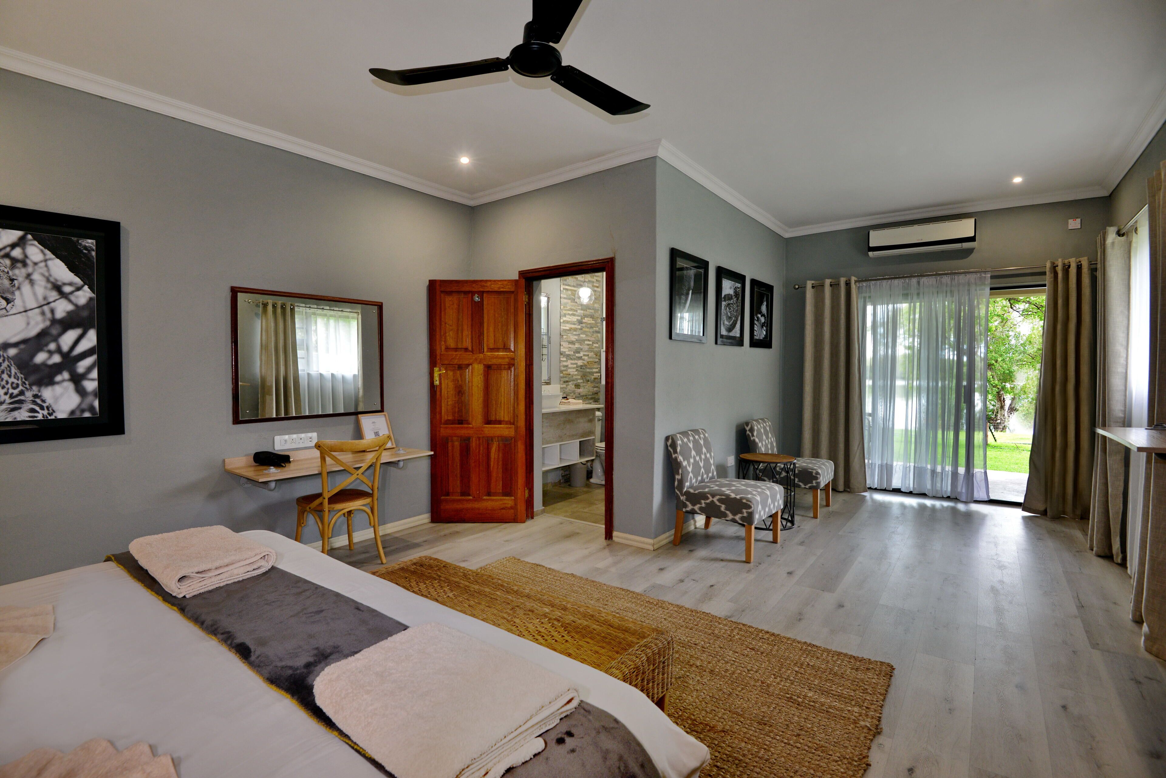 Habitación de hotel con cama, escritorio, silla, ventilador de techo y vistas al exterior.