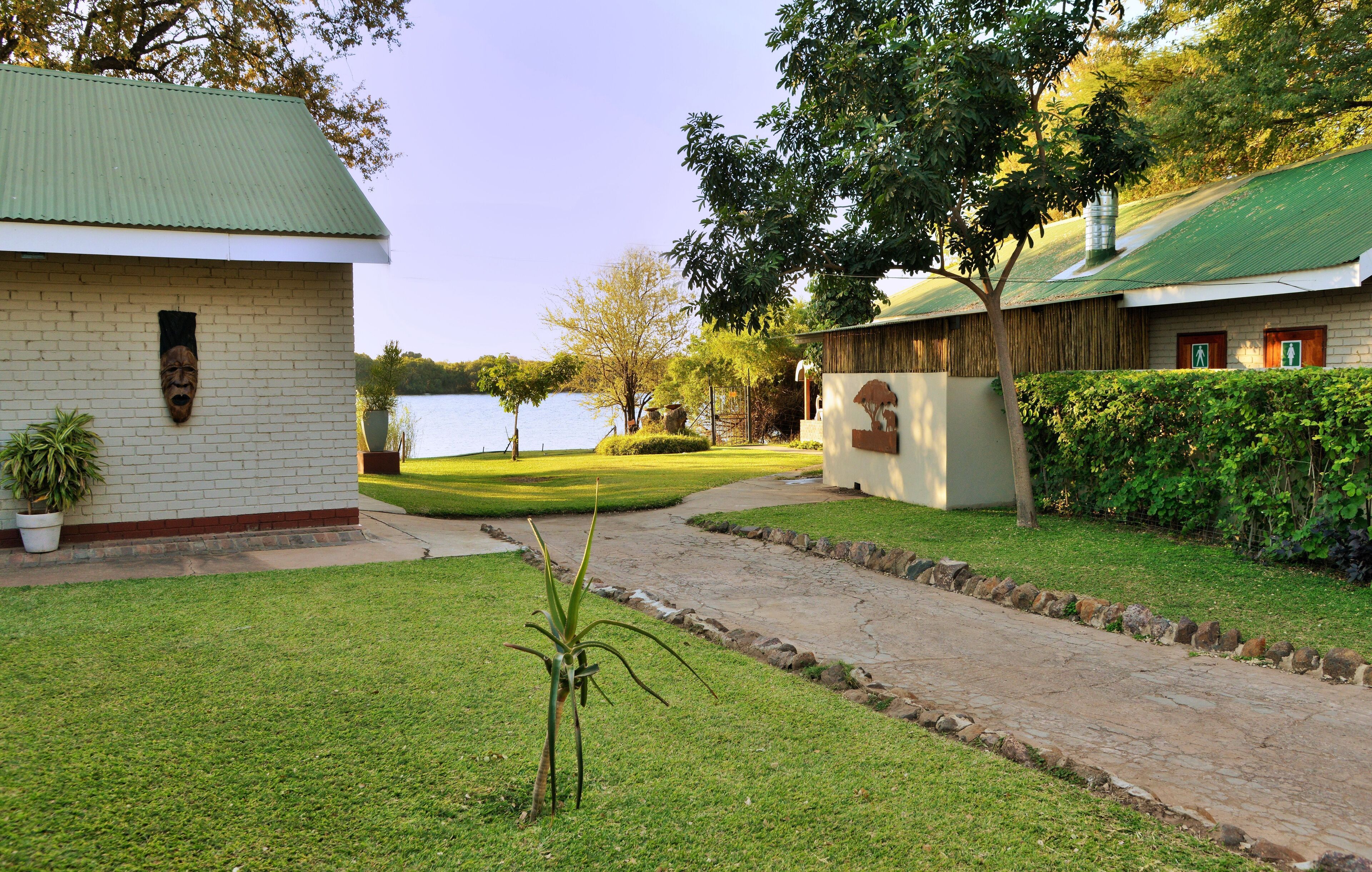 A pathway leading to a building with a green roof, a grassy lawn, and a body of water in the background.