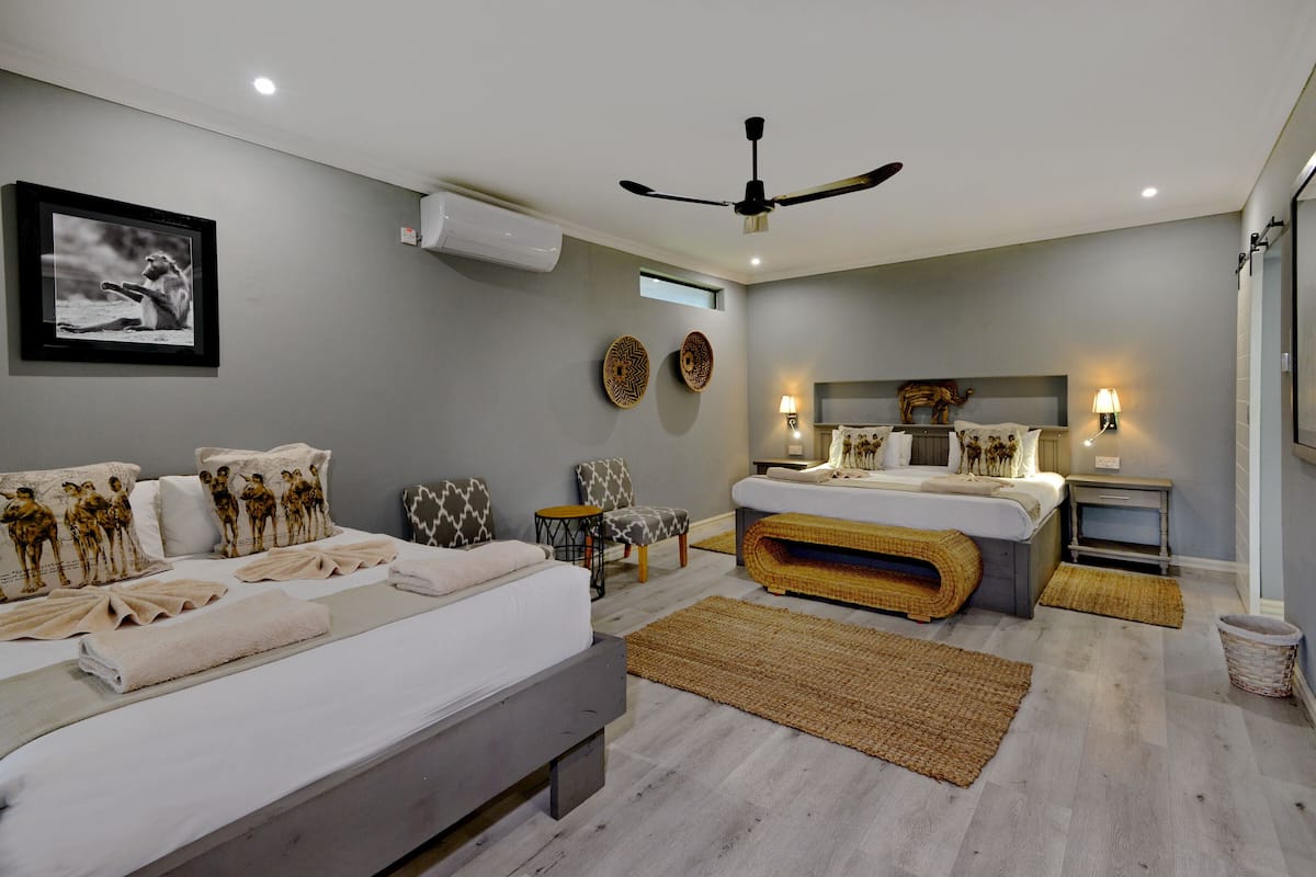 A modern bedroom with a large bed, a smaller bed, a ceiling fan, and a wall-mounted air conditioner.