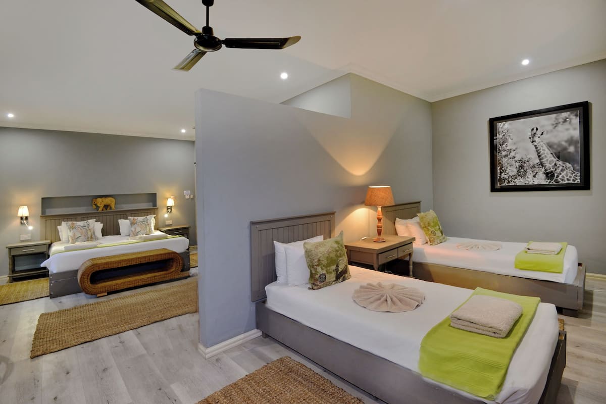 A modern hotel room with two beds, a ceiling fan, and a large framed picture on the wall.