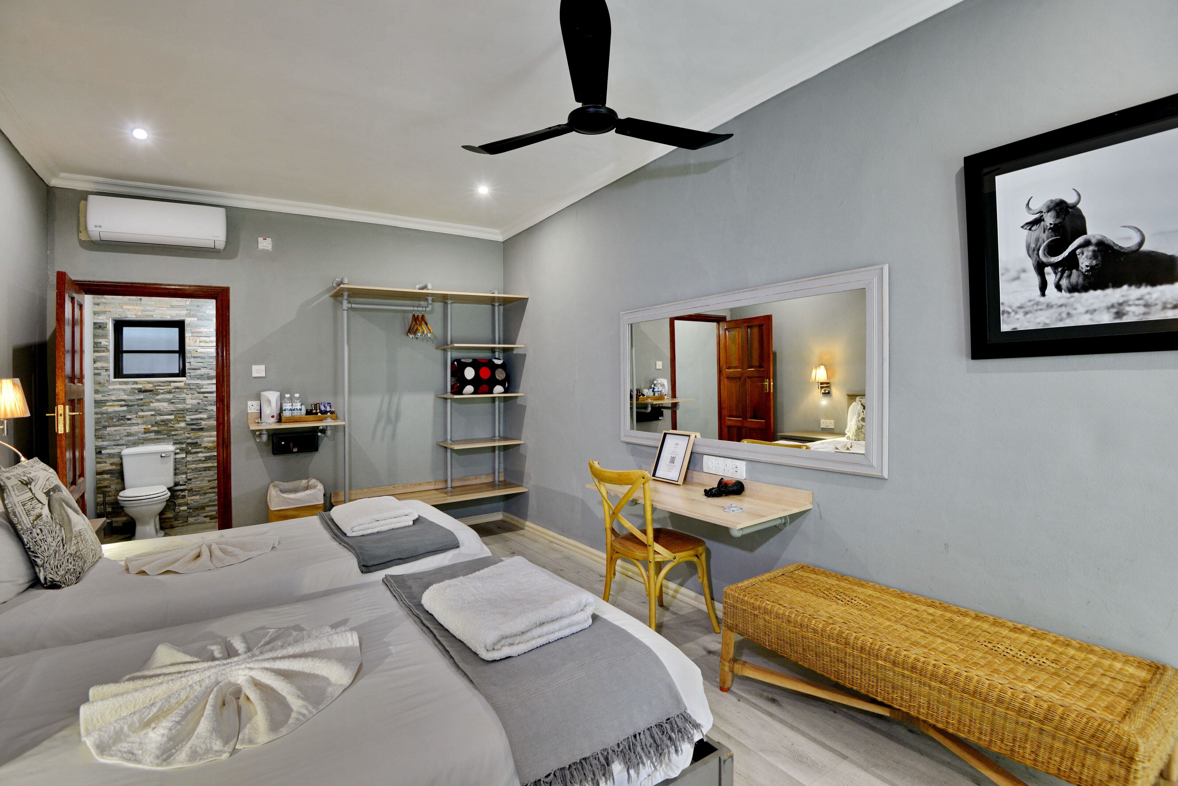 A hotel room with a bed, a desk, a chair, a mirror, and a ceiling fan.