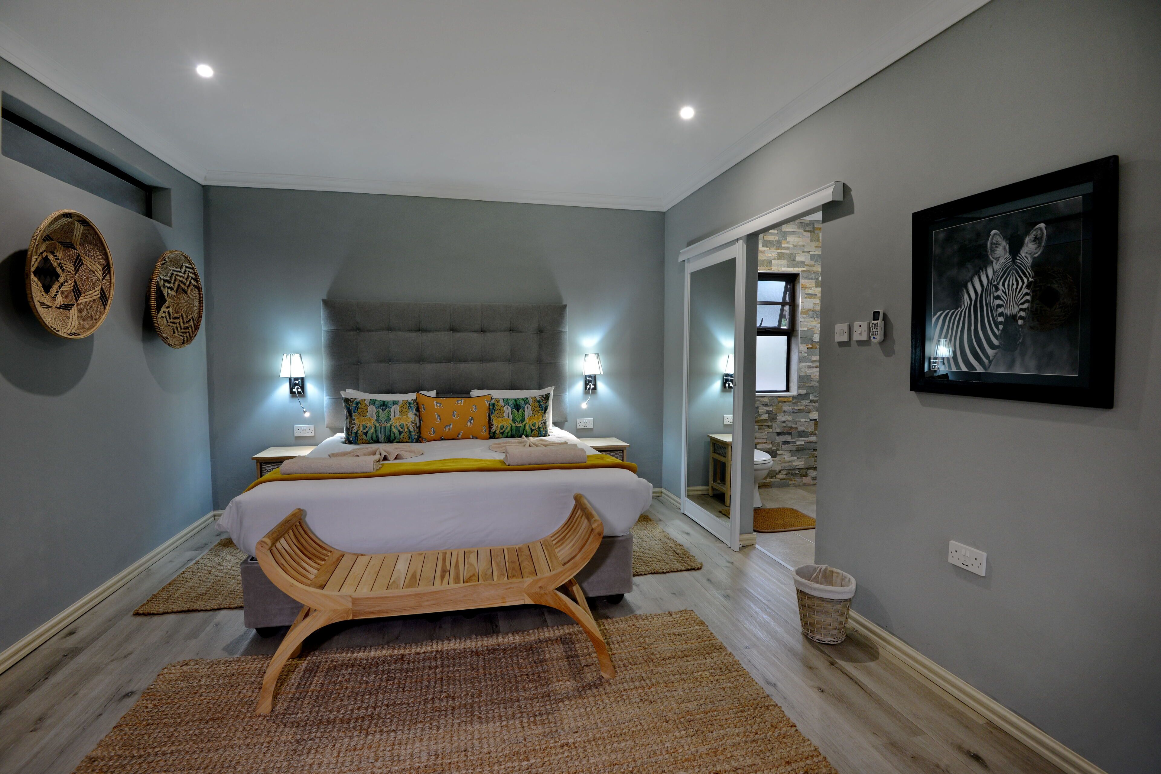 Une chambre à coucher avec un lit, un banc en bois, deux lampes fixées au mur et une œuvre d’art encadrée accrochée au mur.