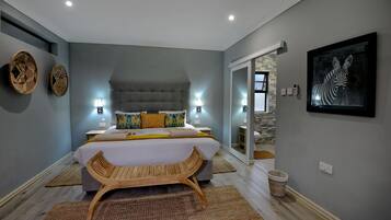 Une chambre à coucher avec un lit, un banc en bois, deux lampes fixées au mur et une œuvre d’art encadrée accrochée au mur.