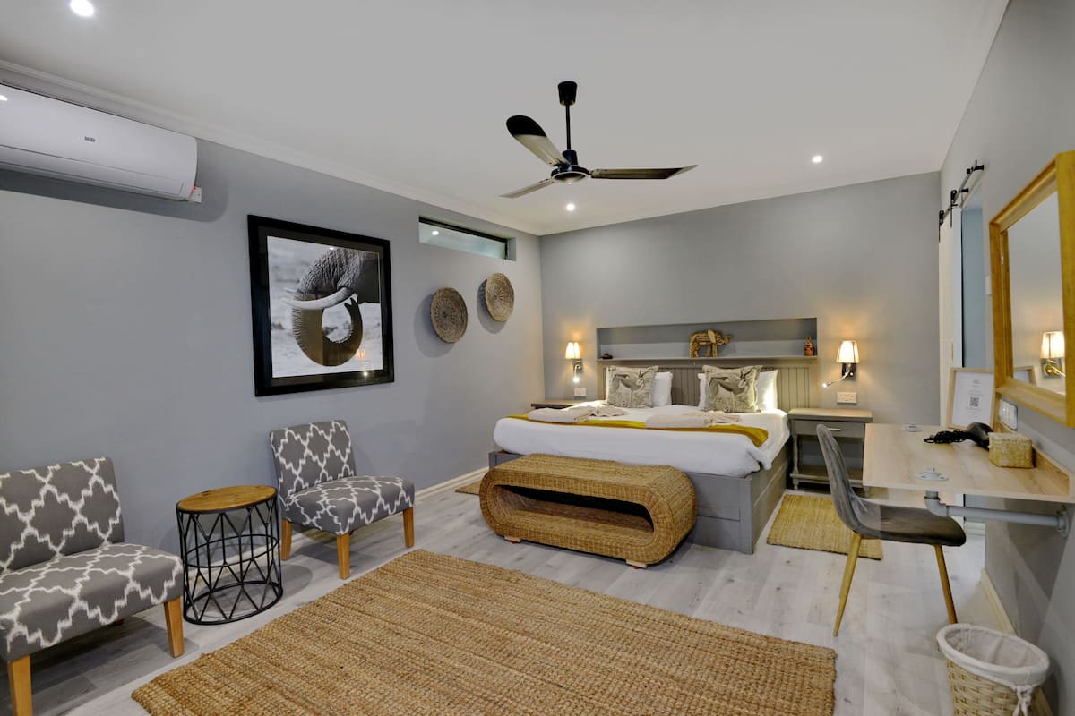 A modern bedroom with a bed, two chairs, a desk, and a ceiling fan.