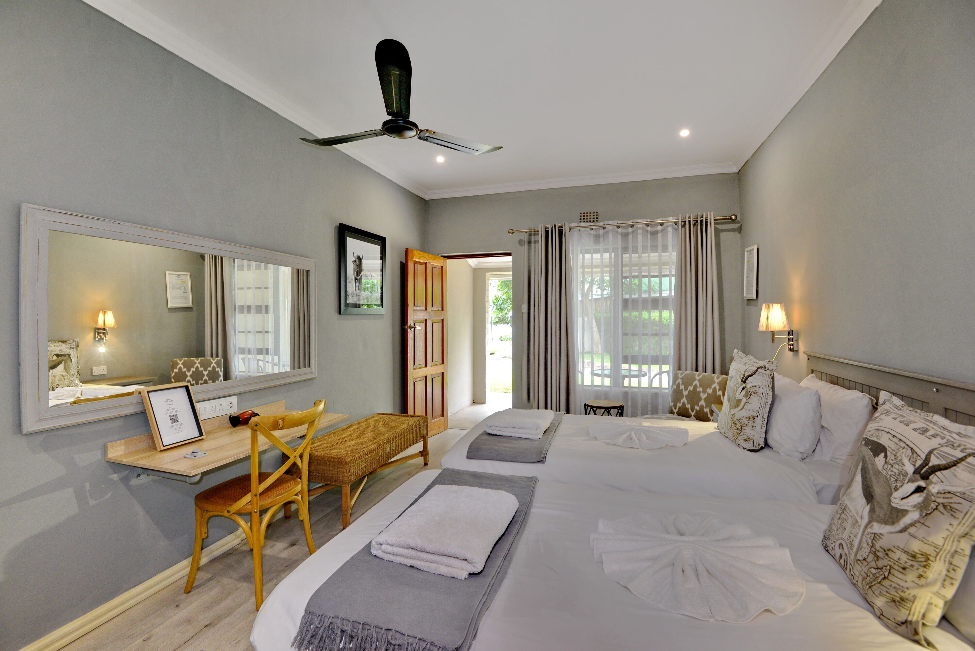 Habitación de hotel con una cama grande, un escritorio, una silla, un ventilador de techo y una ventana con cortinas.