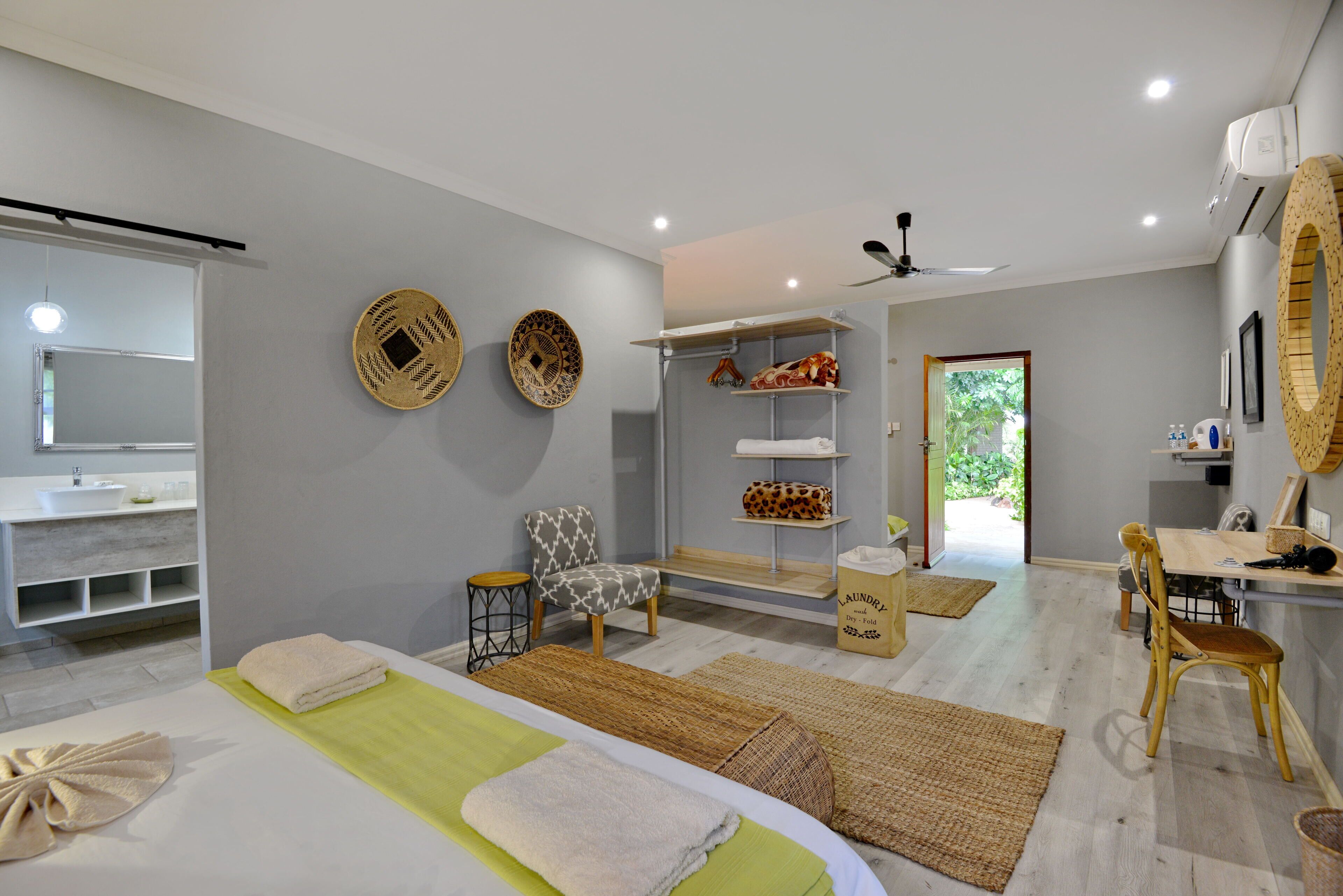 A modern spa room with a bed, towels, a chair, a vanity with a sink, shelves with towels, and a view of the outdoors.