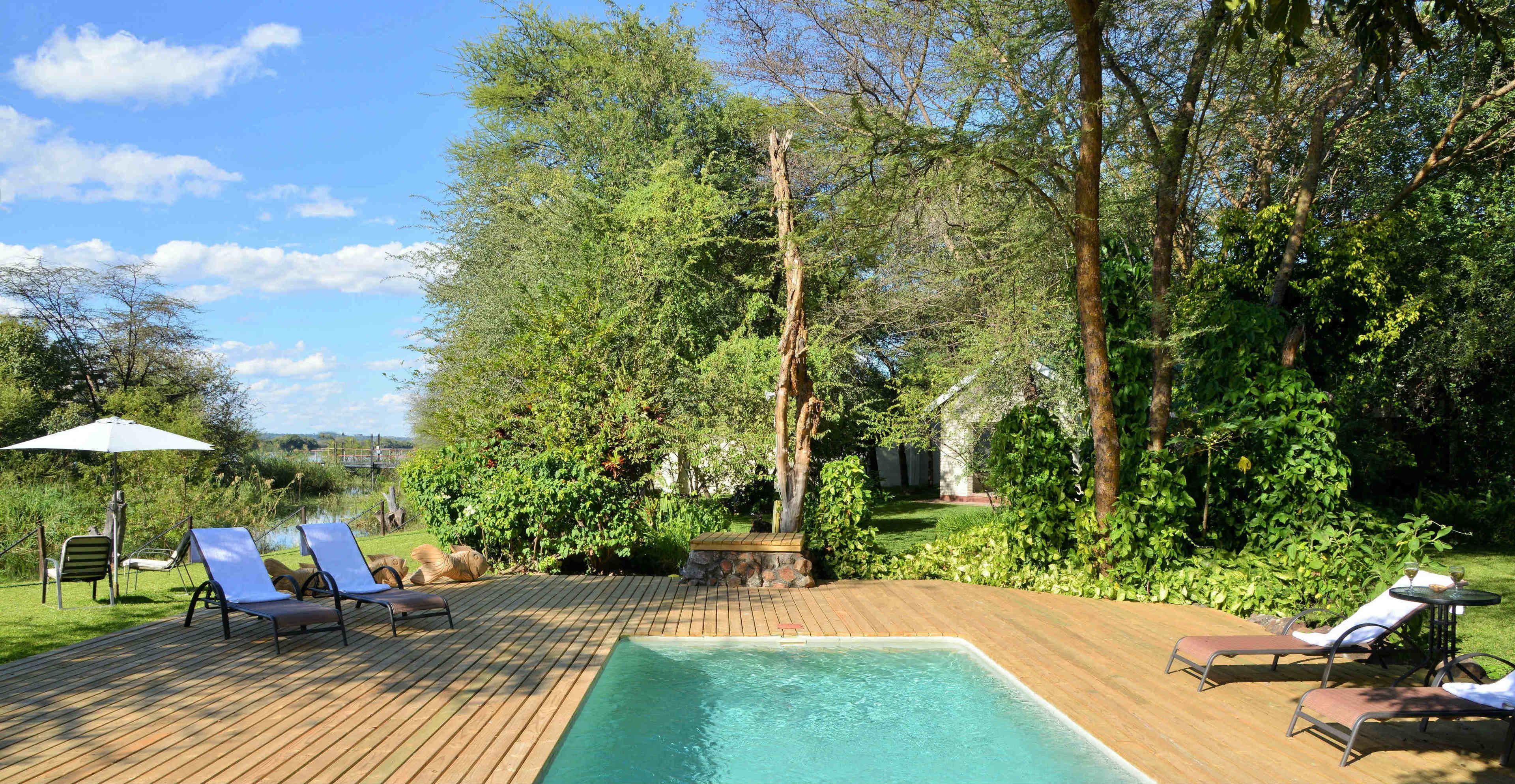 Eine Holzterrasse mit Swimmingpool, Liegestühlen und einem Gartenbereich mit Bäumen und Sträuchern.