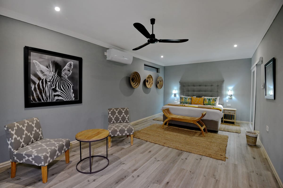 A modern bedroom with a bed, a ceiling fan, a framed zebra artwork, and a small seating area with two chairs and a table.