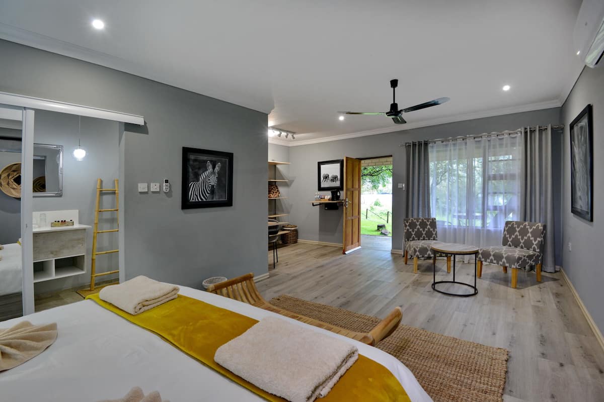 A modern hotel room with a bed, a sitting area with chairs, a small table, and a ceiling fan.