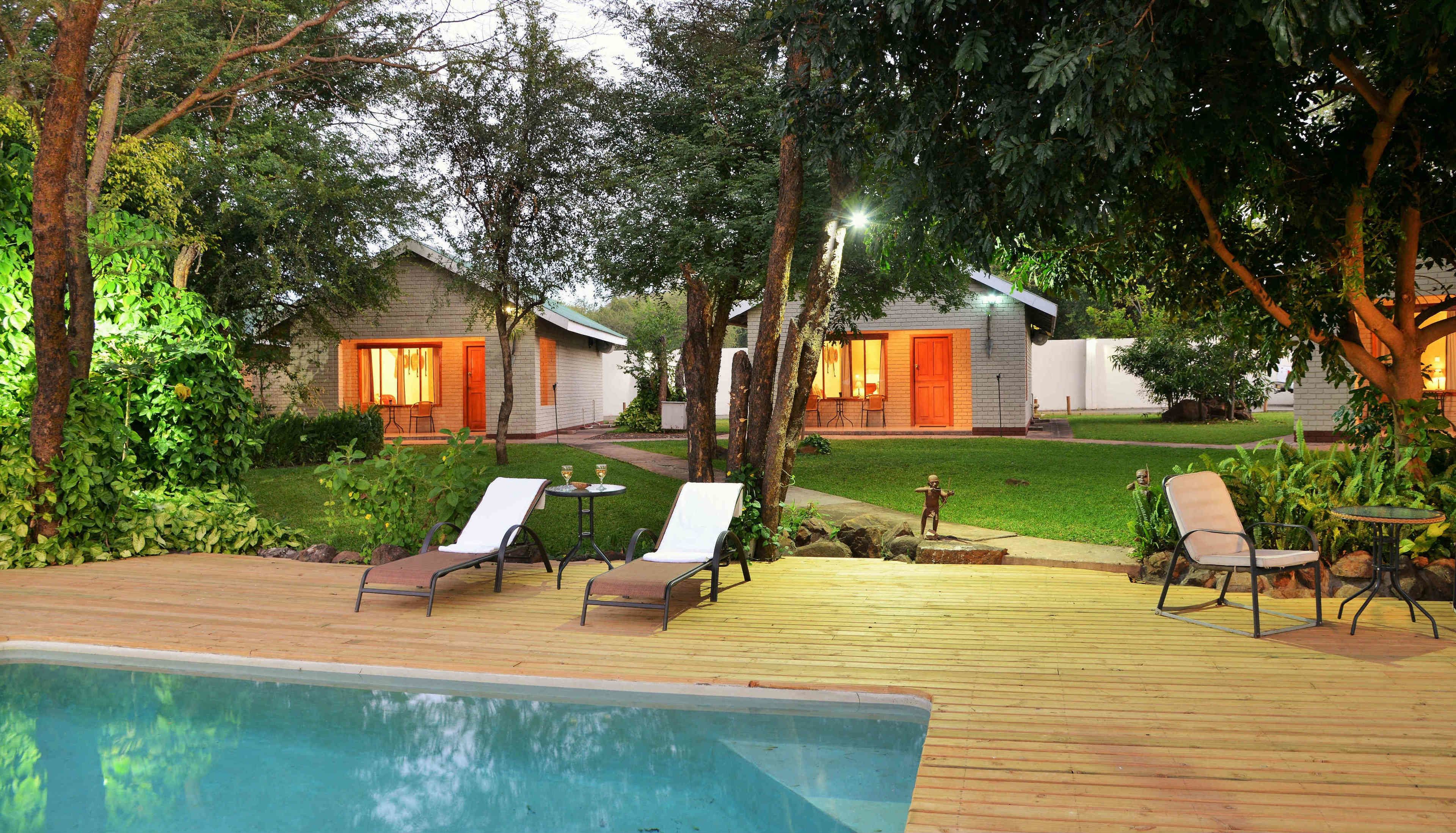 A poolside area with lounge chairs, a small pool, and two guest houses with outdoor lighting.