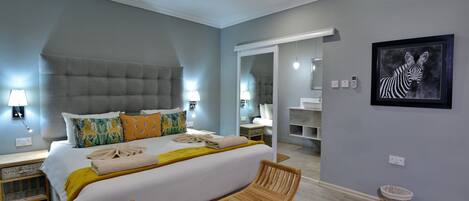 A modern bedroom with a large bed, bedside lamps, a wooden bench, a mirror, and a framed zebra artwork.