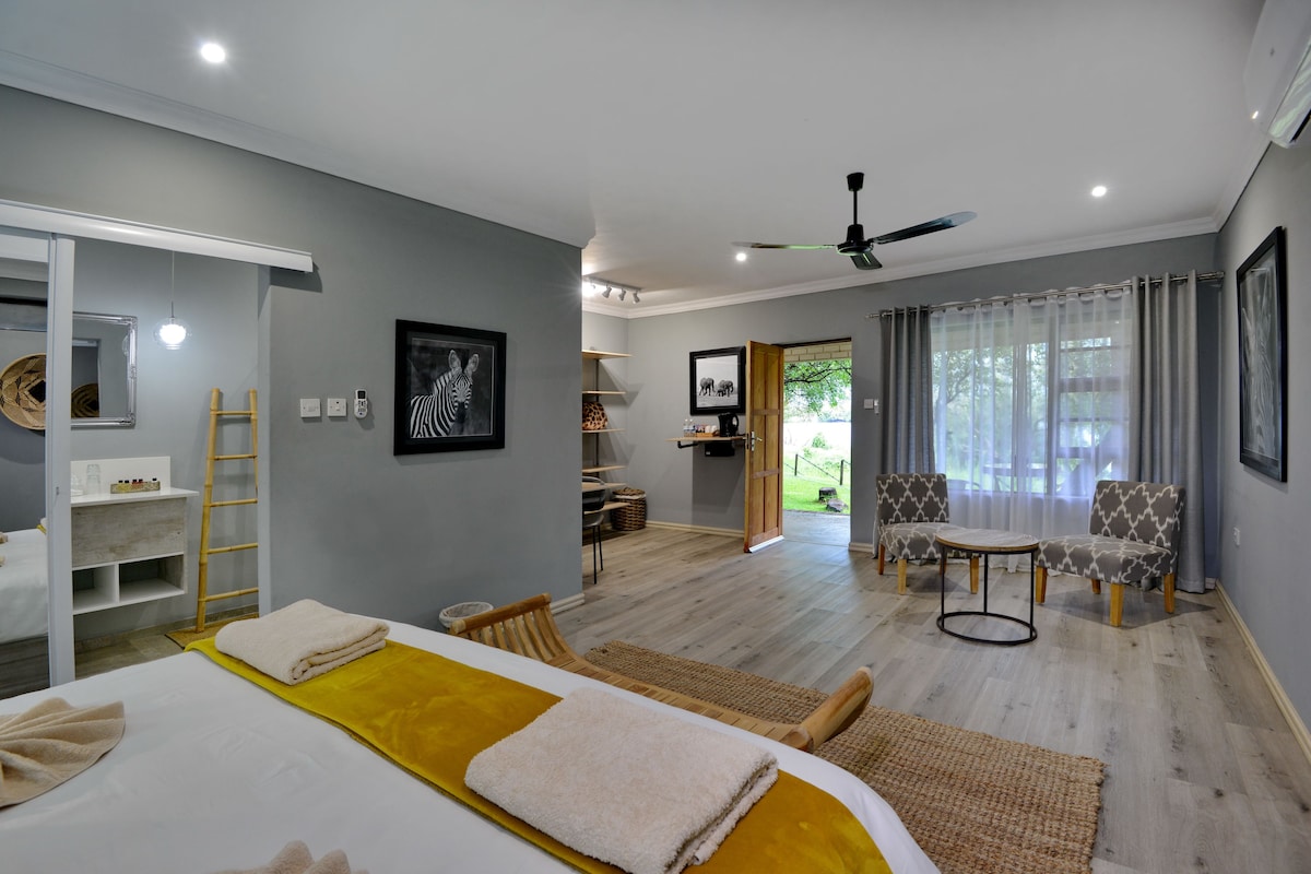 A modern hotel room with a bed, a sitting area with chairs, a small table, and a ceiling fan.