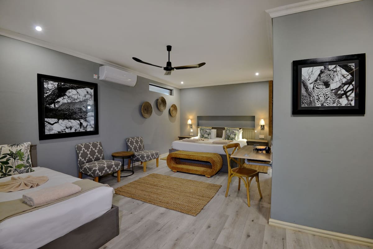 A modern bedroom with a bed, two chairs, a desk, and a ceiling fan.