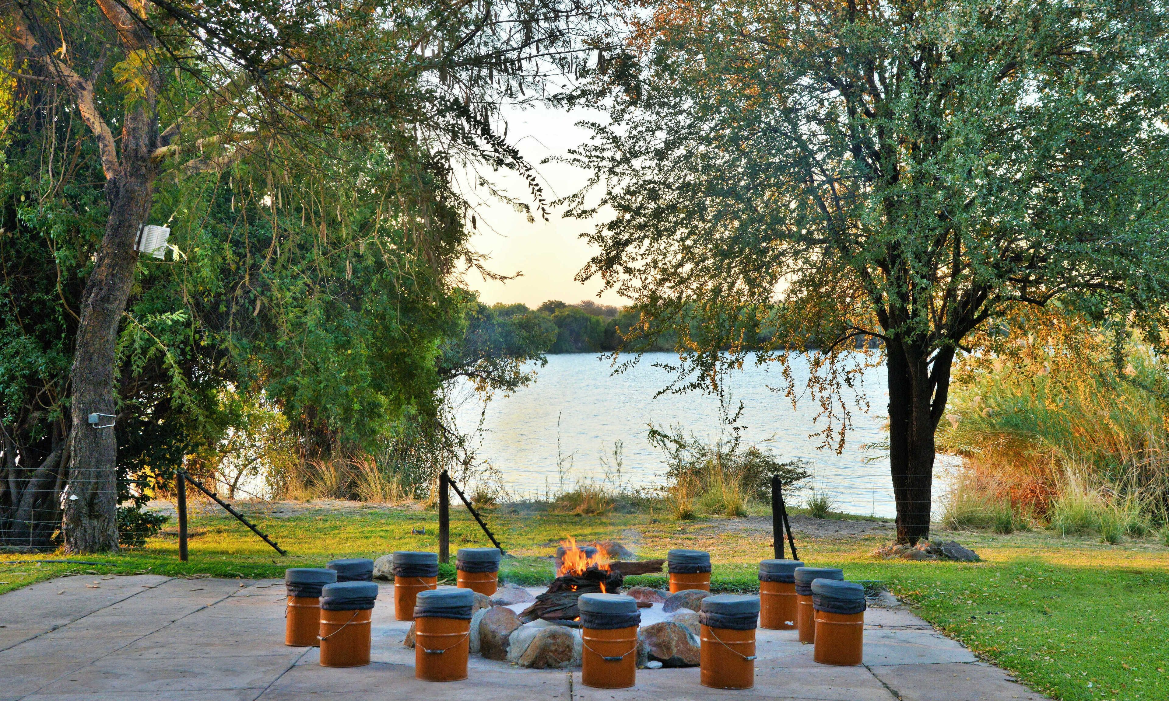 A lakeside outdoor seating area with fire pits and metal barrels.