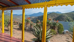 A covered outdoor area with yellow pillars, surrounded by desert plants and a view of distant mountains.
