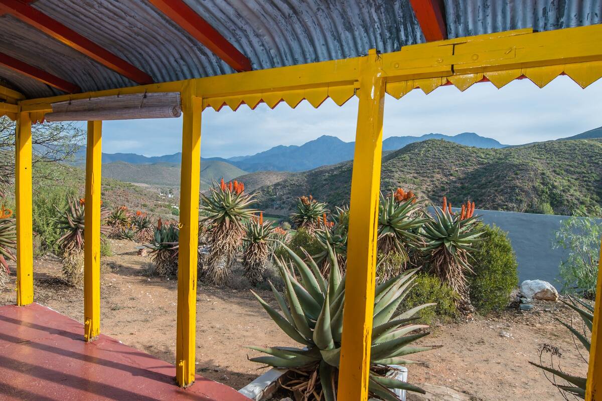 A covered outdoor area with yellow pillars, surrounded by desert plants and a view of distant mountains.