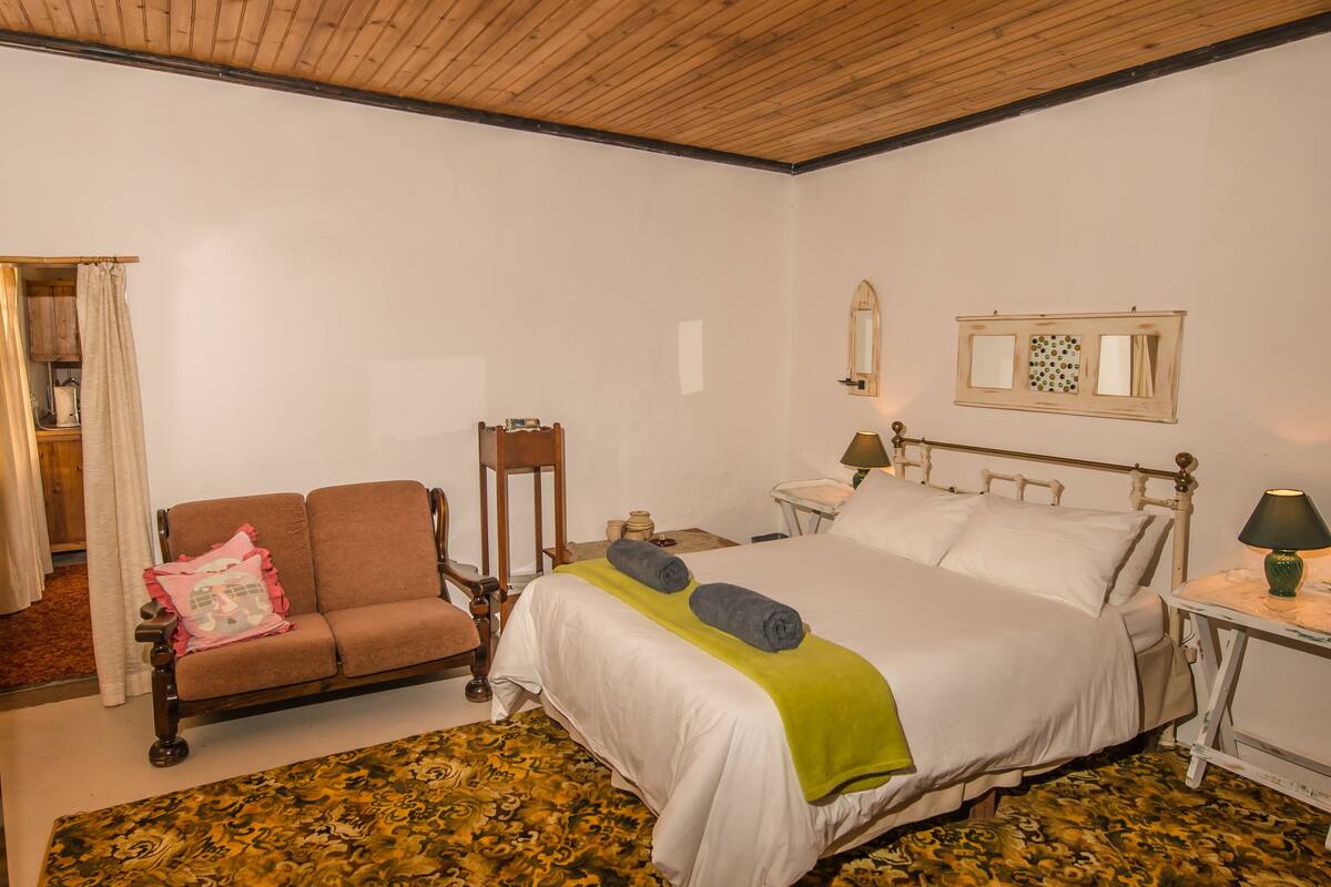 A bedroom with a bed, a chair, a nightstand, a mirror, and a window.