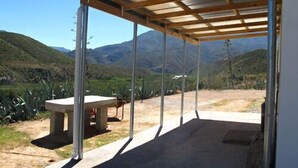 A covered outdoor area with a concrete bench and a table, surrounded by a mountainous landscape.