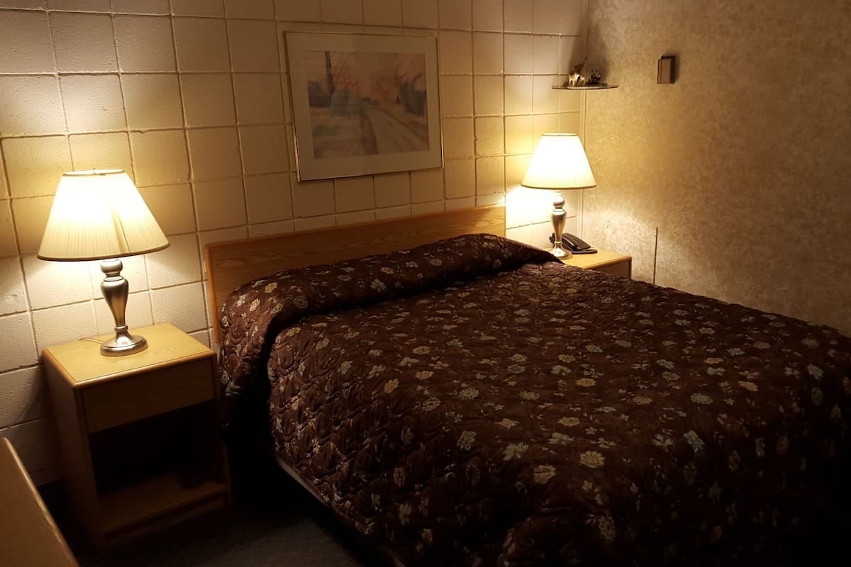 A bed with a floral bedspread, two bedside lamps, a wooden nightstand, and a framed picture on the wall.