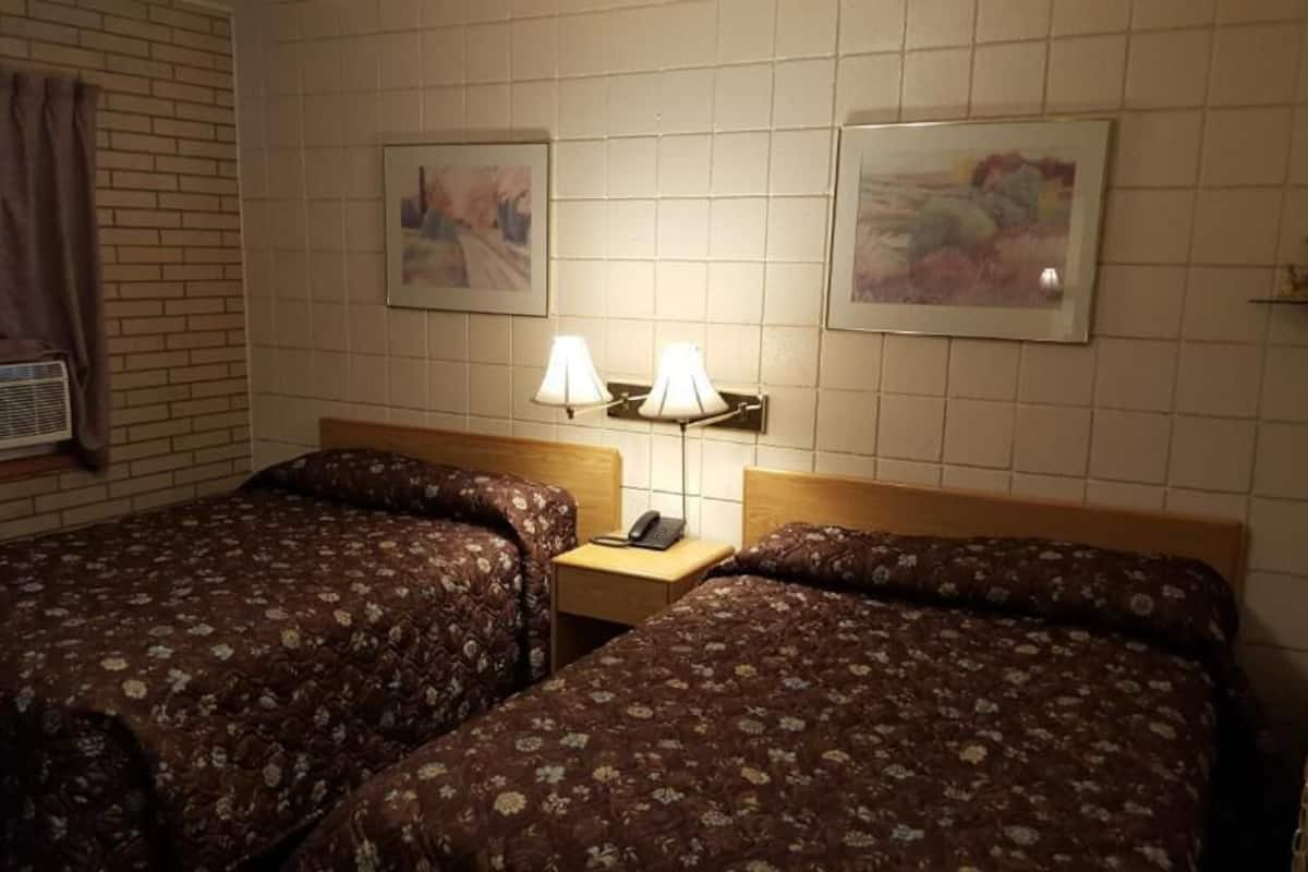 A hotel room with two beds, a nightstand with a lamp, and artwork on the walls.