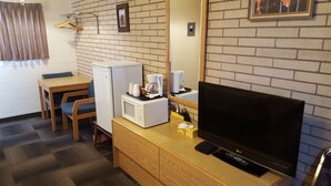 A hotel room with a wooden desk, a microwave, a coffee maker, a TV, and a mirror. - Safari Inn Motel (Swift Current)