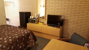 A hotel room with a bed, a TV, a microwave, a coffee maker, and a desk with a chair. - Safari Inn Motel (Swift Current)