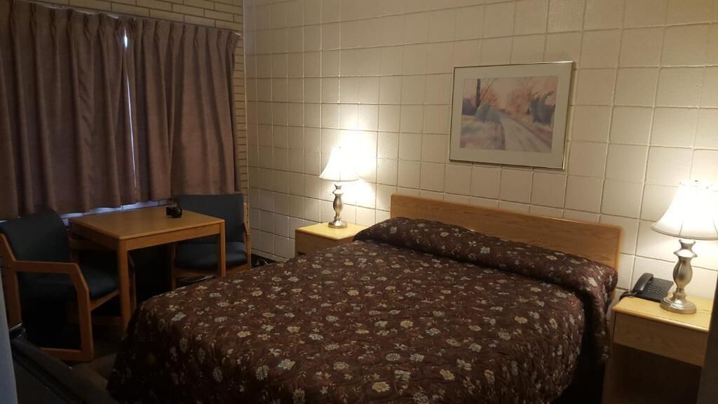 A hotel room with a bed, a desk, a chair, two bedside lamps, and a painting on the wall.