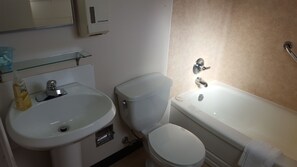 A bathroom with a white sink, toilet, and bathtub. There is a glass shelf above the sink and a towel hanging on the bathtub.