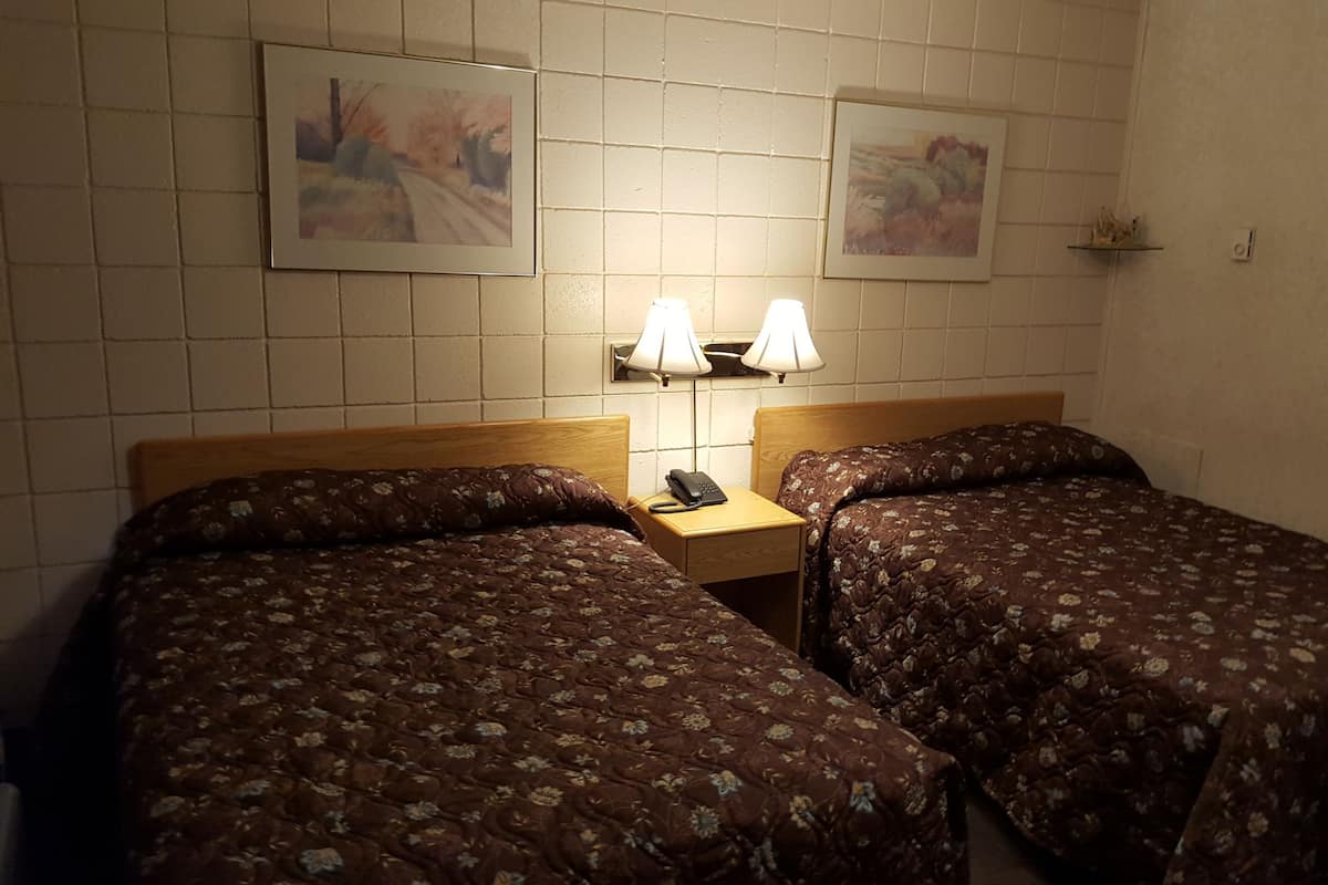 A hotel room with two beds, each with floral-patterned bedding. There are two wall-mounted lamps on a nightstand between the beds.