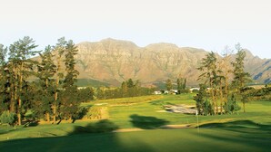 A golf course with a mountain backdrop, a flagstick, and a water hazard. - Rest Chabivin Self Catering (Stellenbosch)
