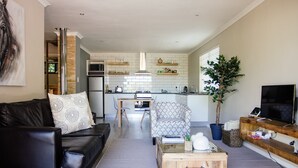 A modern living room with a black leather sofa, a patterned armchair, a wooden coffee table, and a television on a wooden stand. - Rest Chabivin Self Catering (Stellenbosch)