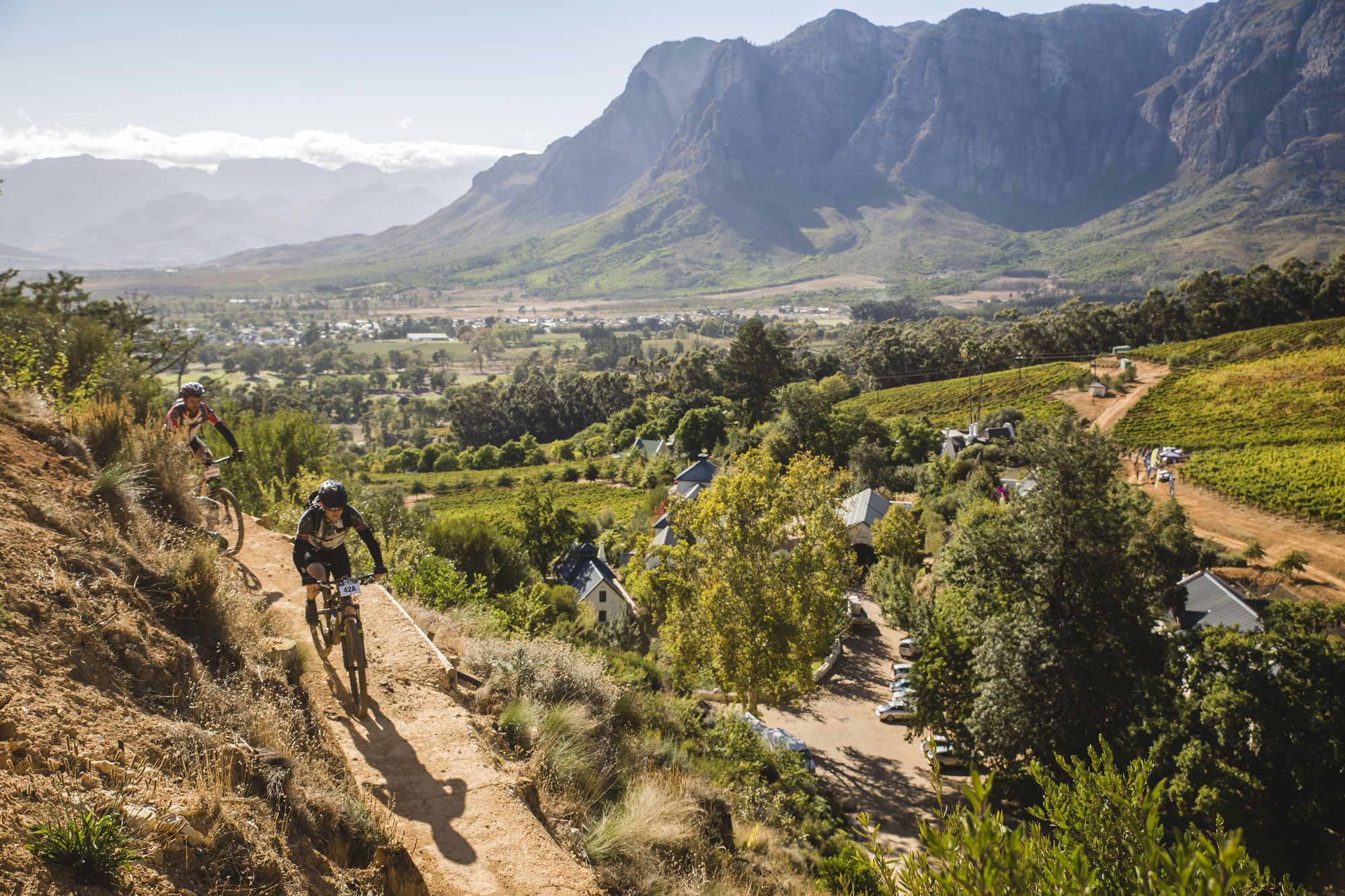 A mountain biking trail with a view of a valley, houses, and vineyards.