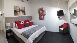 Moderni hotellihuone, jossa on sänky, televisio, tuoli ja taideteoksia seinillä.
