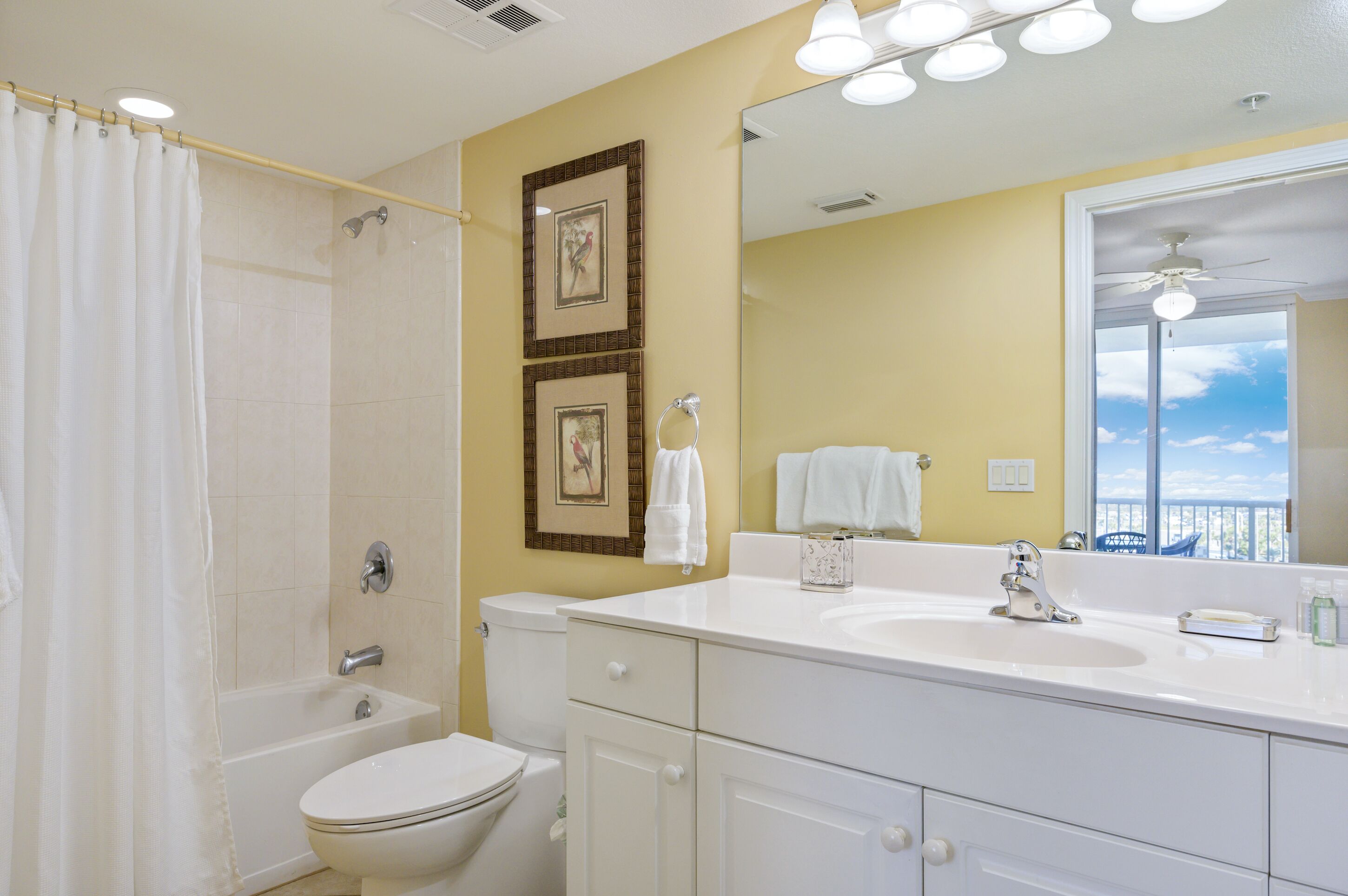 A bathroom with a bathtub, toilet, and sink. There are framed pictures on the wall and a large mirror above the sink.