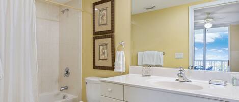 A bathroom with a bathtub, toilet, and sink. There are framed pictures on the wall and a large mirror above the sink.