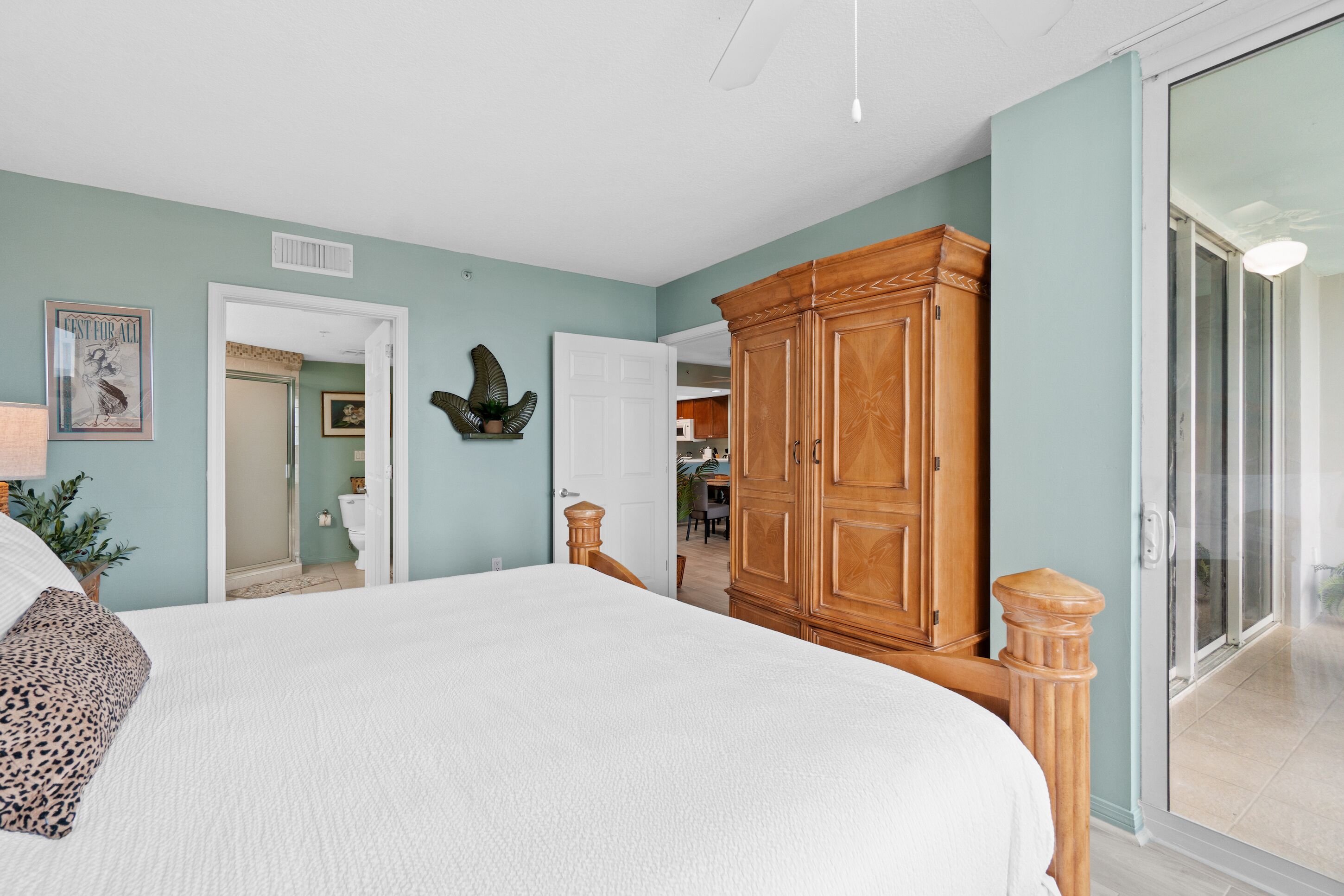 A bedroom with a large bed, wooden wardrobe, and a sliding glass door leading to a balcony.