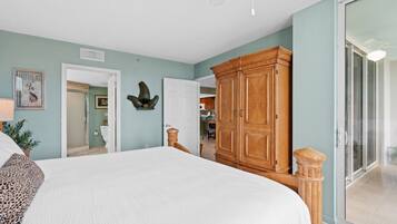A bedroom with a large bed, wooden wardrobe, and a sliding glass door leading to a balcony.