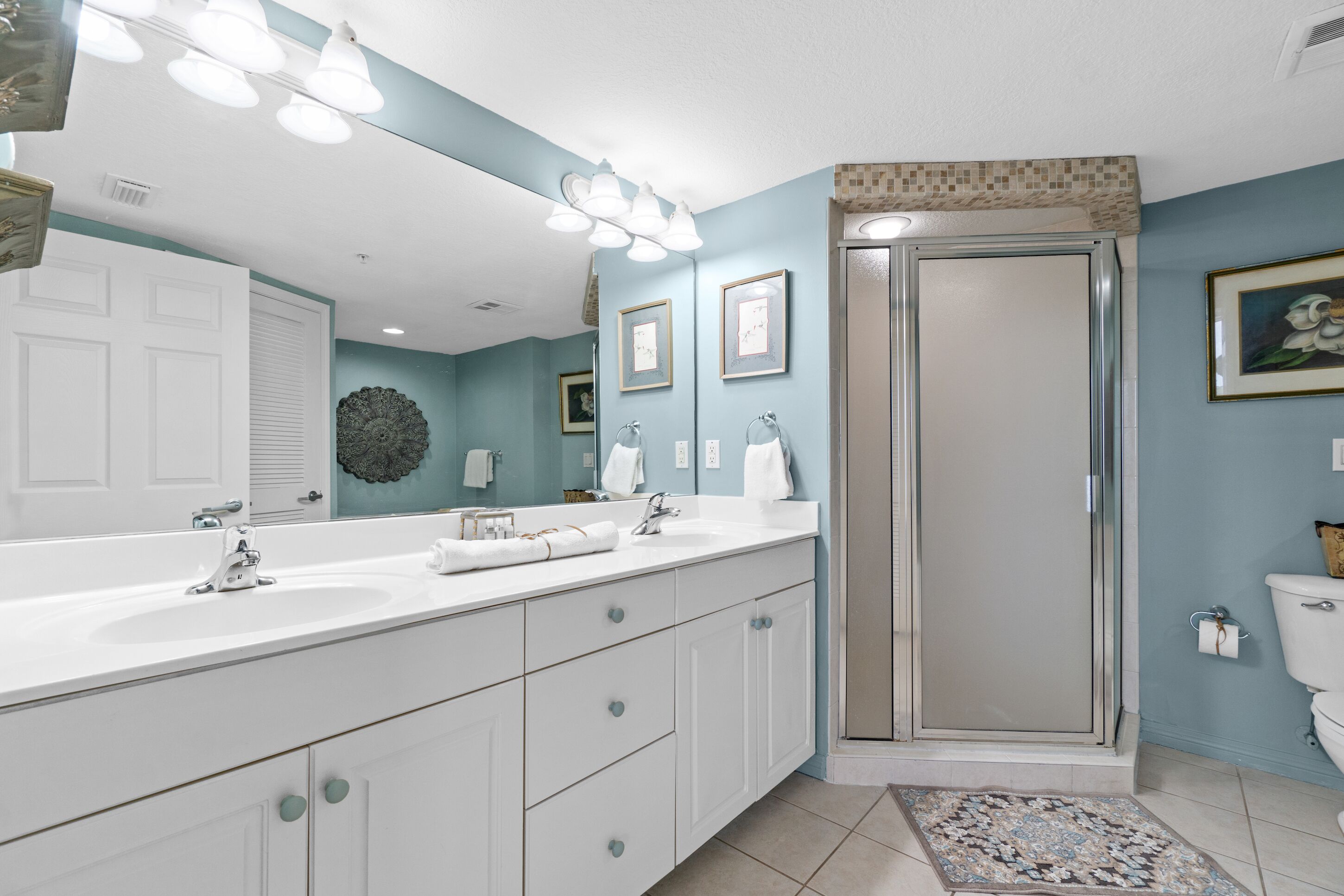 Une salle de bain avec un grand miroir, deux lavabos, une douche et des toilettes.