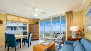 A spacious living area with a balcony, a dining table with chairs, a sofa, and a ceiling fan. - Destin West Resort by Panhandle Getaways (Fort Walton Beach)