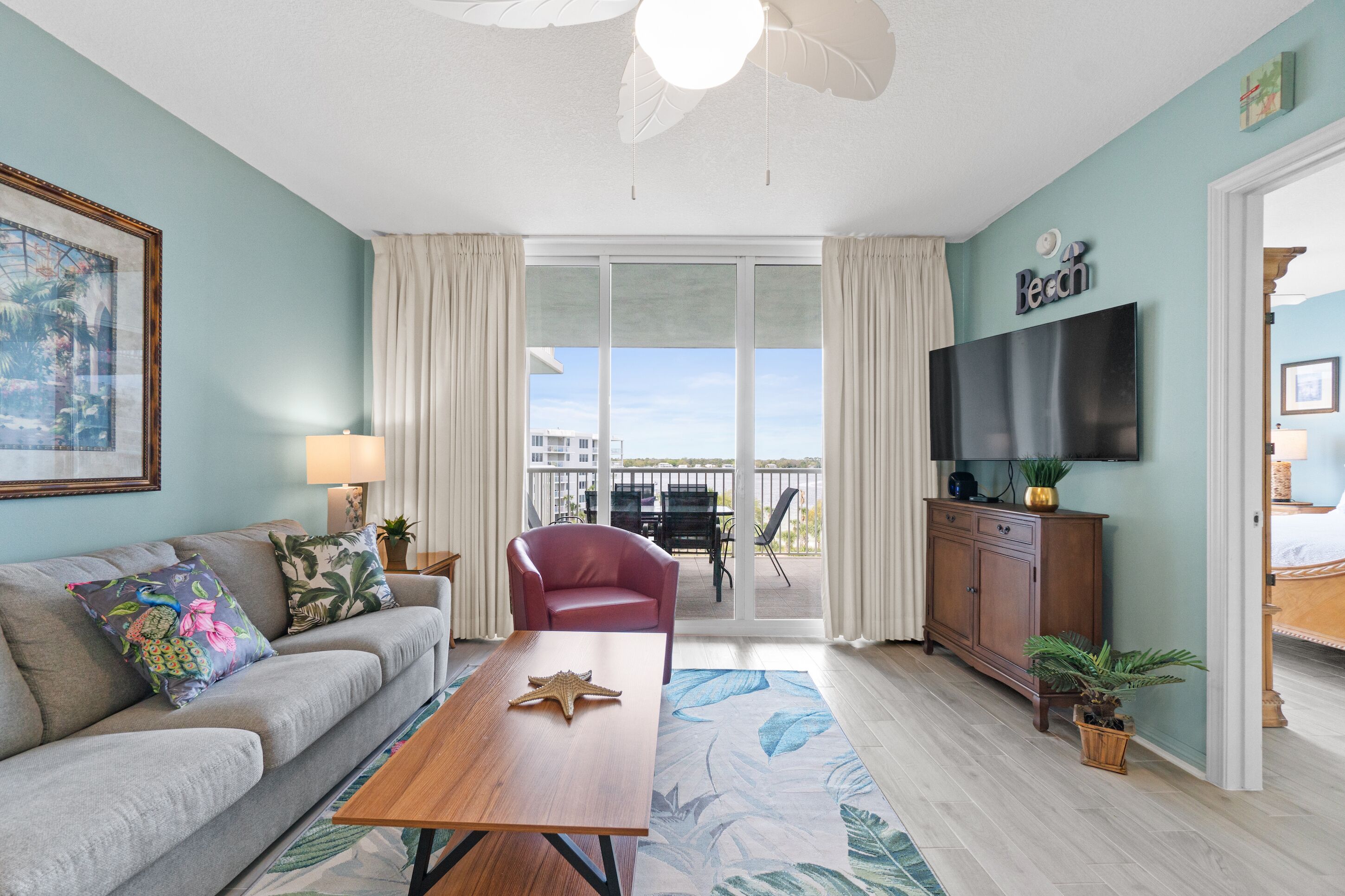 A living room with a sofa, a coffee table, a red chair, a TV, and a balcony with a view.