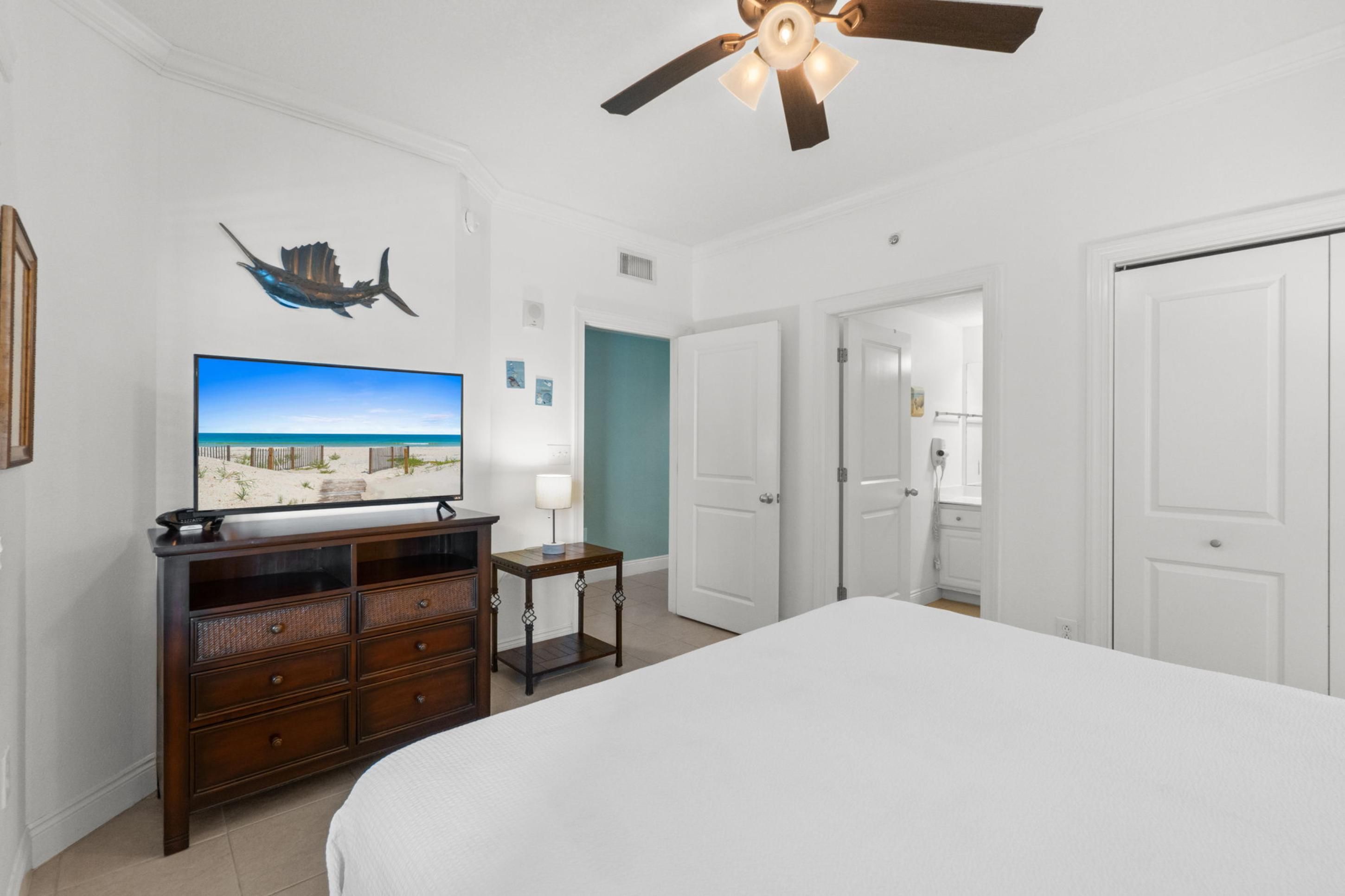 Ein Hotelzimmer mit einem Bett, einem Fernseher, einem Deckenventilator und einer Tür zu einem anderen Raum.