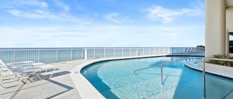 A pool area with a clear view of the ocean, lounge chairs, and a railing.