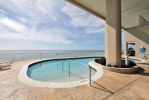 Piscina com vista para o oceano, cercada por um deck ladrilhado e um corrimão.