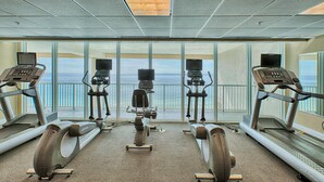 Un gimnasio con cintas de correr y bicicletas estáticas, amplias ventanas con vista al océano y un alto techo con tragaluz.