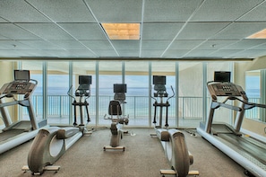A gym with treadmills and stationary bikes, large windows with a view of the ocean, and a high ceiling with a skylight.