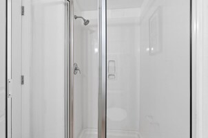 A glass-enclosed shower area with a handheld showerhead, a door with a handle, and a wall-mounted control panel.
