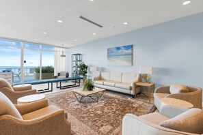 A spacious living area with a large window overlooking a beach, a sofa, armchairs, a coffee table, and a side table with a lamp. - Palazzo Beach Resort by Panhandle Getaways (Panama City Beach)