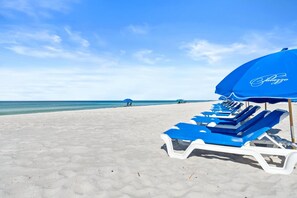 A beach with rows of blue sun loungers and a blue umbrella with the brand name visible. - Palazzo Beach Resort by Panhandle Getaways (Panama City Beach)