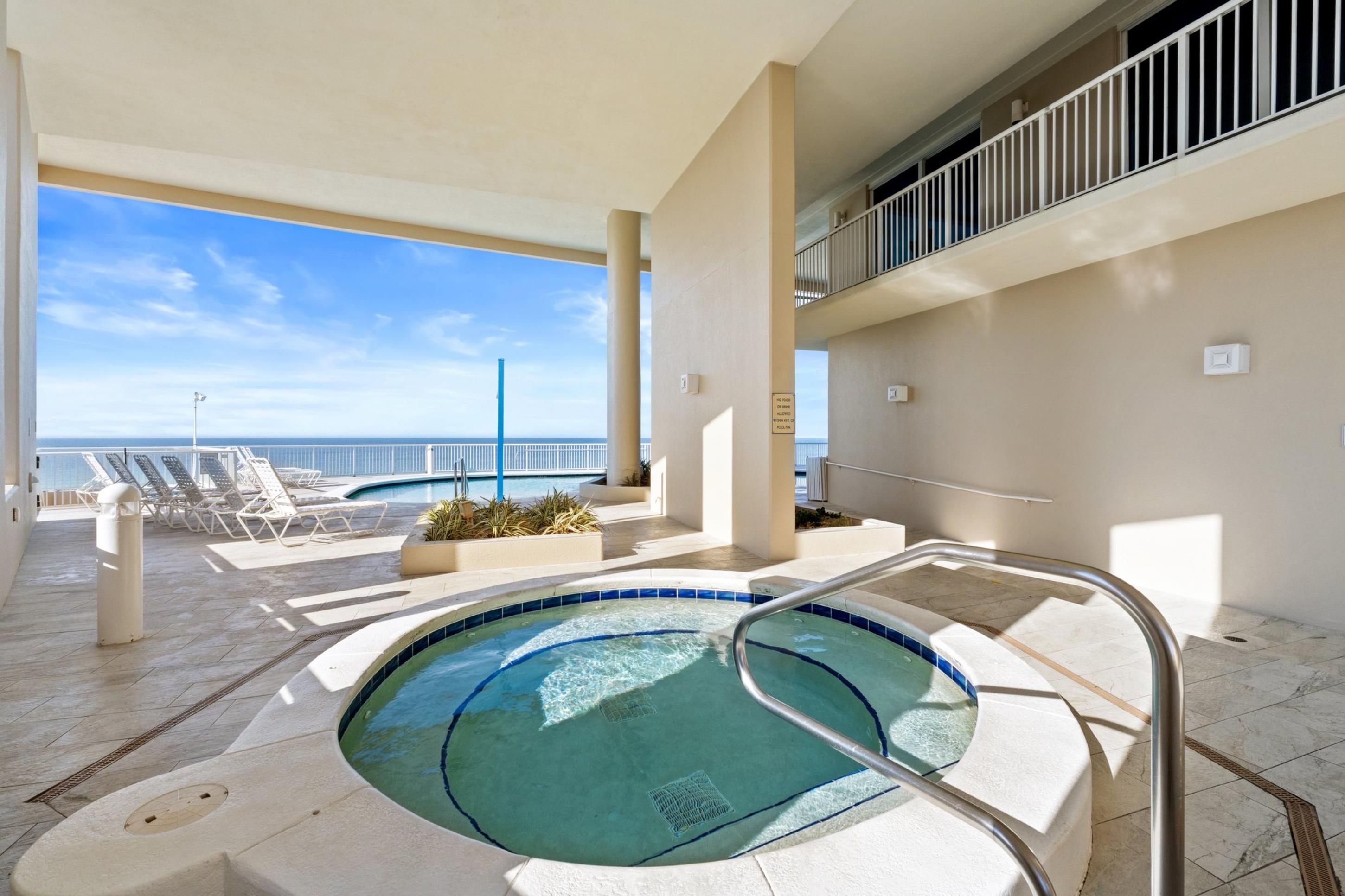 A pool area with a hot tub, lounge chairs, and a view of the ocean.