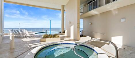 A pool area with a hot tub, lounge chairs, and a view of the ocean.